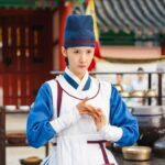 Person in traditional Korean attire, hands clasped.