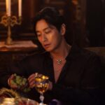 Man holding grapes in dimly lit room.