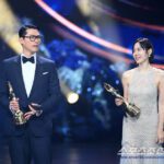 Two people holding awards on stage.