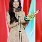 Woman holding award on stage, smiling.