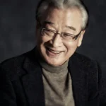 Smiling elderly man with glasses and sweater.
