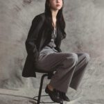 Woman sitting on stool in suit.