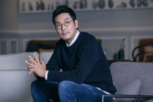 Man sitting on a chair, wearing glasses.